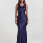 Front full-length studio portrait of the Genevra dark blue maxi dress, featuring a sophisticated draped cowl neckline, a sleeveless cut, and a fluid satin column skirt with structural geometric waist seams.