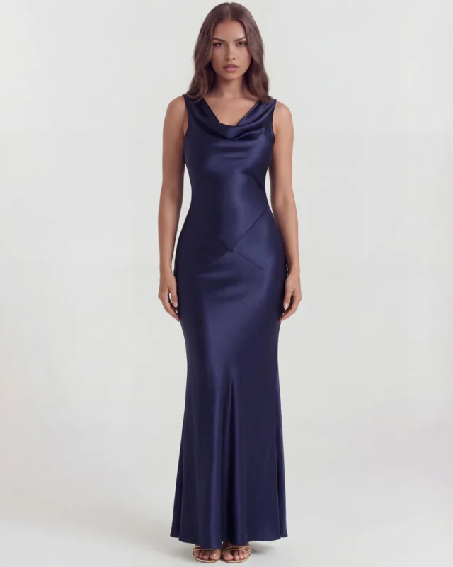 Front full-length studio portrait of the Genevra dark blue maxi dress, featuring a sophisticated draped cowl neckline, a sleeveless cut, and a fluid satin column skirt with structural geometric waist seams.