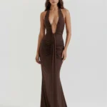 Front full-length portrait of the Alessandra brown maxi gown in deep chocolate jersey, featuring an ultra-low plunging halter neck, structural hip ruching, and a dramatic vertical front drape.