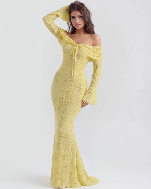 Three-quarter front full-length shot of the light yellow lace formal dress with a hand raised to the hair, emphasizing the draped bardot neckline and curve-skimming mermaid silhouette.