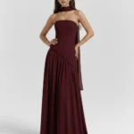 Front full-length portrait of the Caterina burgundy maxi dress, showcasing a strapless corset bodice with an asymmetrical dropped-waist seam, a matching fabric neck choker, and a gathered floor-length skirt.