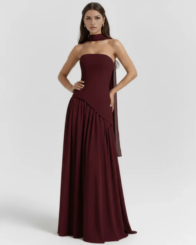 Front full-length portrait of the Caterina burgundy maxi dress, showcasing a strapless corset bodice with an asymmetrical dropped-waist seam, a matching fabric neck choker, and a gathered floor-length skirt.