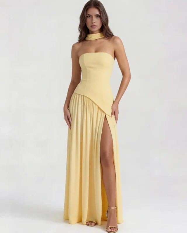 Front full-length studio shot of the Caterina maxi gown in pastel butter yellow, featuring a structured strapless corset bodice, an asymmetrical dropped-waist seam line, a matching yellow choker, and a high-slit skirt.