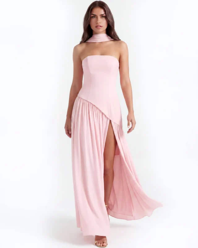 Front full-length studio portrait of the Caterina pink maxi dress, showcasing a strapless corset bodice with an asymmetrical dropped-waist seam, a matching fabric neck choker, and a gathered floor-length skirt with a high thigh slit.