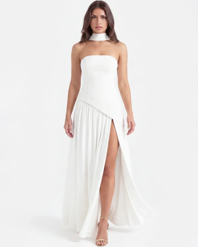 Front full-length portrait of the Caterina white maxi dress, featuring a strapless corset bodice with a sharp asymmetrical dropped-waist seam, a matching white fabric neck choker, and a flowing floor-length skirt with a high side leg slit.