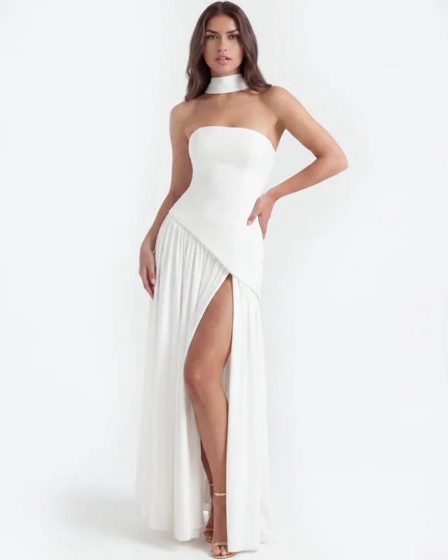 Front full-length studio shot of the white strapless corset formal gown with a hand-on-hip pose, highlighting the modern diagonal waist seam, high thigh-high slit, and elegant gold high heels.