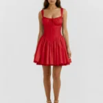 Front full-length studio portrait of the Celeste red mini dress, featuring a vibrant scarlet cotton construction, a cinched corset waist, gathered puff sleeves, and matching gold high-heeled sandals.