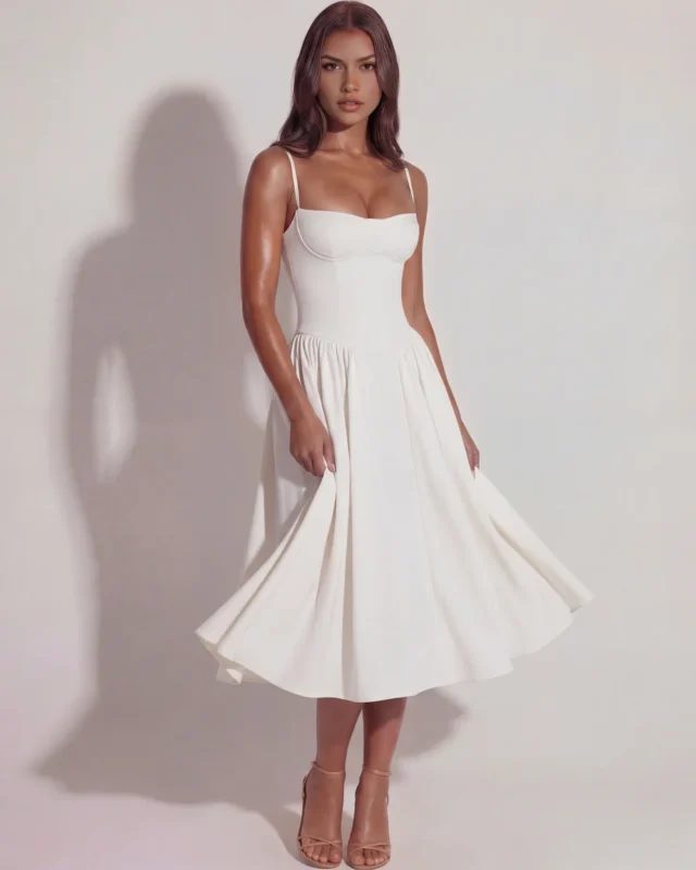 Front view of a romantic white bustier midi dress showcasing the flowing silhouette, architectural drop waist, and thin adjustable spaghetti straps on structured premium twill fabric.