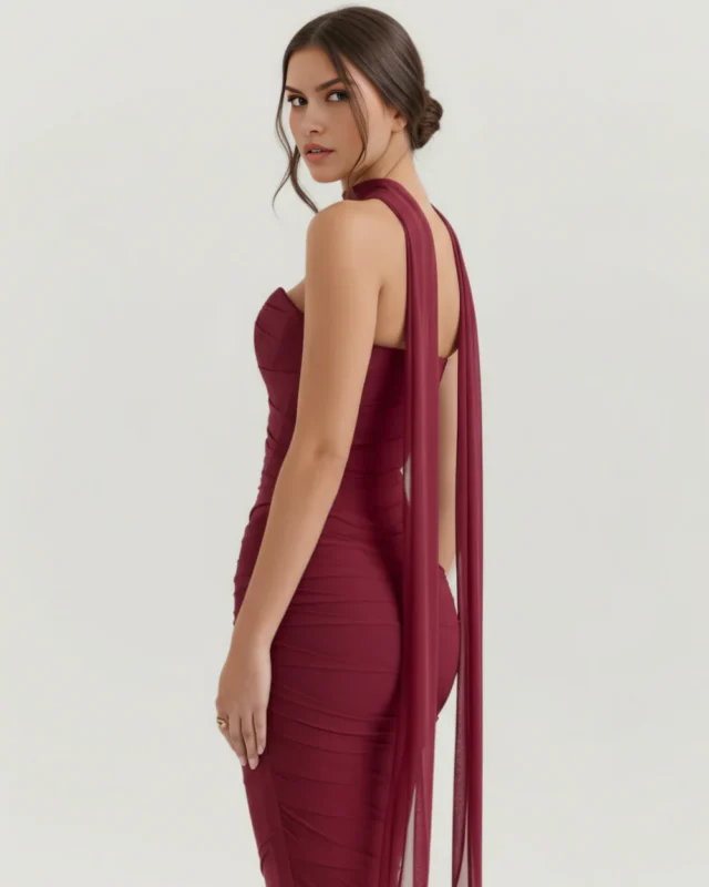 Side profile perspective of the burgundy mesh evening gown, emphasizing the form-fitting hourglass silhouette and long, flowing chiffon scarf panels trailing elegantly down the model's back.