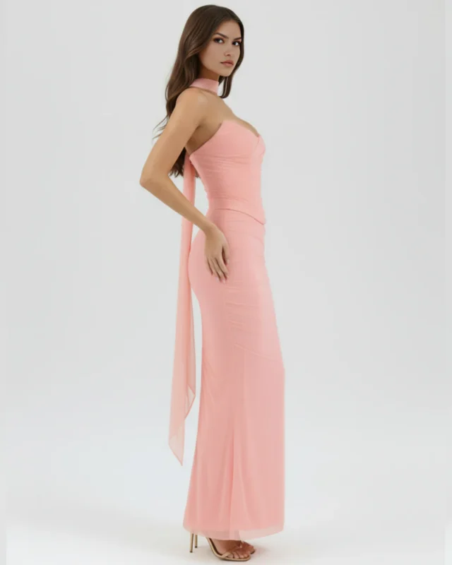 Side profile full-length view of the pastel pink formal gown, showcasing the elongated column shape and the graceful movement of the sheer chiffon trailing neck sashes.