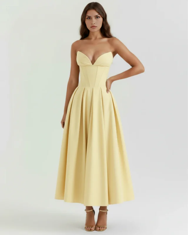 Front full-length studio shot of the Mirabella light yellow midi dress, featuring a soft pastel lemon hue, a structured strapless boned bodice, a voluminous pleated skirt, and metallic gold stiletto sandals.
