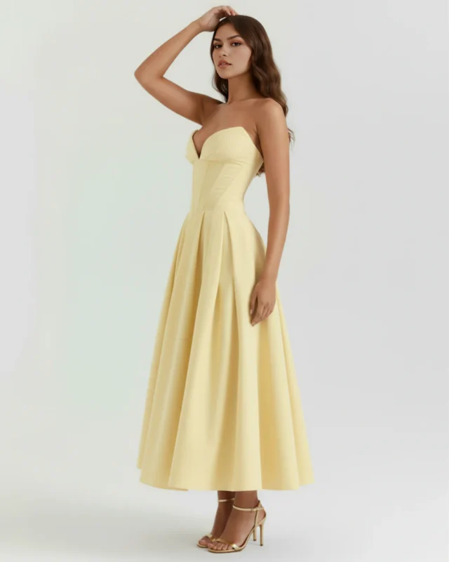 Full-body side angle view of the model wearing the light yellow strapless corset dress with one hand raising toward her hair, showcasing the structural fit of the pointed sweetheart bust-line.
