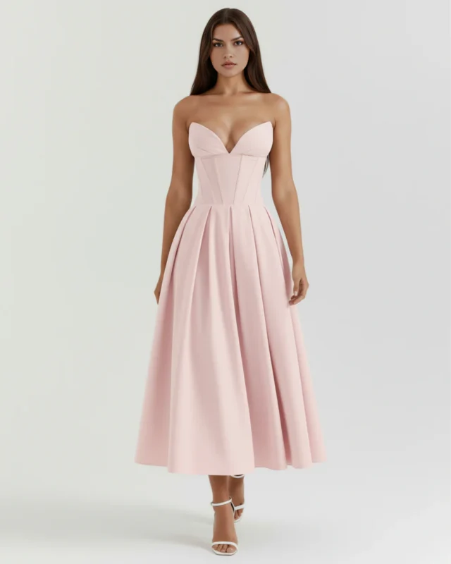 Front full-length studio portrait of the Mirabella pink midi dress, showcasing a structured strapless corset bodice with a plunging sweetheart neckline, a voluminous pleated A-line skirt, and white strappy high heels.