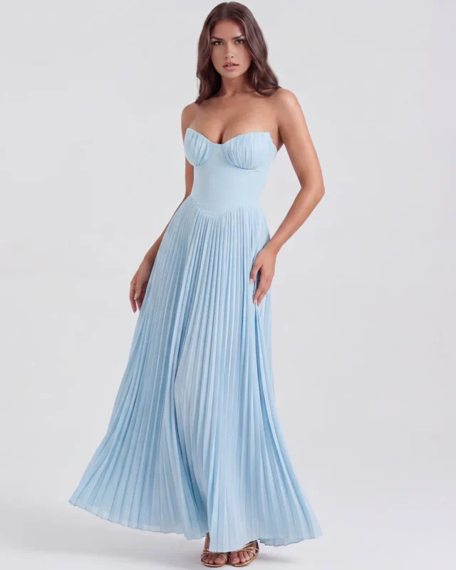 Front three-quarter movement shot of the baby blue strapless formal dress, emphasizing the flowing movement of the micro-pleated column skirt and a glimpse of gold strappy heels.