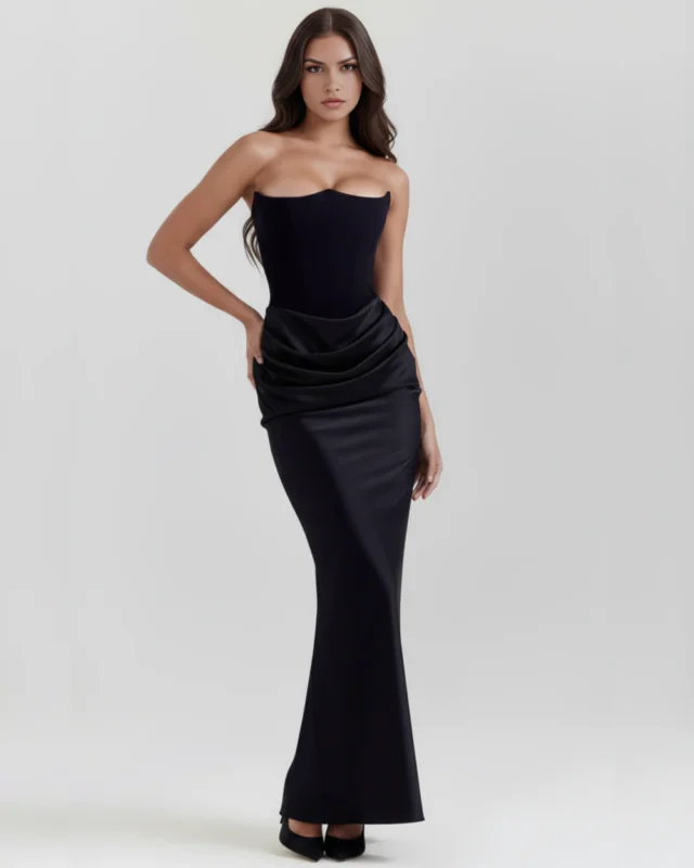 Front full-length view of the Rosalinda strapless corset maxi gown in classic black, showcasing the architectural pointed bust-line, structured column silhouette, and heavy satin cowl-draped hip detail.