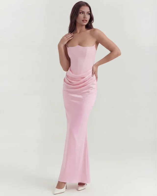 Front full-length view of the Rosalinda strapless corset maxi gown in soft blush pink, showcasing the architectural curved neckline, tailored drop-waist torso, and fluid satin column skirt paired with cream high heels.