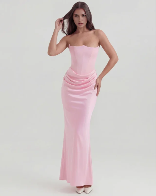 Front full-length shot of a pastel pink strapless satin formal dress with a hand-to-hair pose, emphasizing the layered cowl draping over the hips and a clean, sculpted boutique profile.