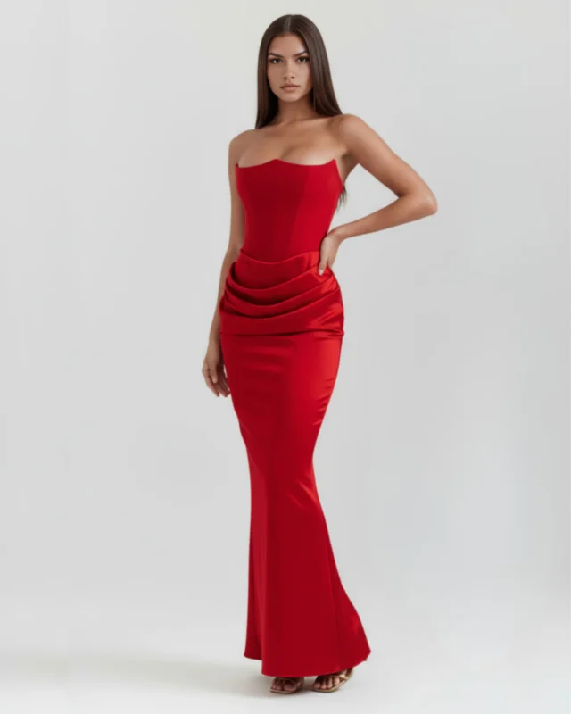 Front full-length oblique shot of the Rosalinda strapless corset maxi gown in vibrant ruby red, showcasing the dramatic pointed bustline, heavy satin hip gathering, and a cinematic sweeping skirt.
