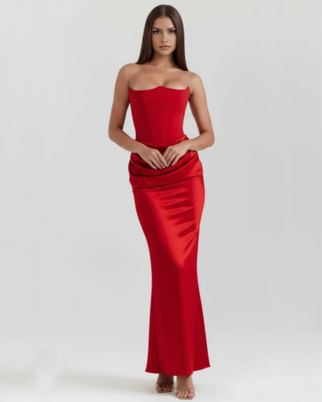 Front full-length portrait of a rich red strapless satin formal gown with clasped hands, highlighting the waist-cinching structure and elegant fluid draping across the lower torso.