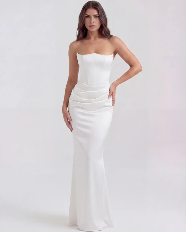 Front full-length shot of the Rosalinda strapless corset maxi gown in pristine ivory white, emphasizing the dramatic pointed bustline, waist-cinching structure, and heavy satin cowl-draped hip gathering.