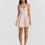 Front full-length view of a blush pink corset mini dress featuring structural cupped underwired supportive panels, slim spaghetti straps, and a short high-volume flared A-line skirt with a white tulle petticoat trim.