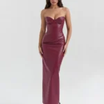 Front full-length studio view of the Victoria burgundy dress in wine-red faux leather, featuring a strapless sweetheart bodice with structured molded cups and a multi-directional draped hip design.
