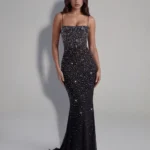 Front full-length studio portrait of the Vivienne black maxi gown, showcasing a straight strapless-style neckline with ultra-thin spaghetti straps and a body-contouring column silhouette encrusted with light-reflecting crystals.